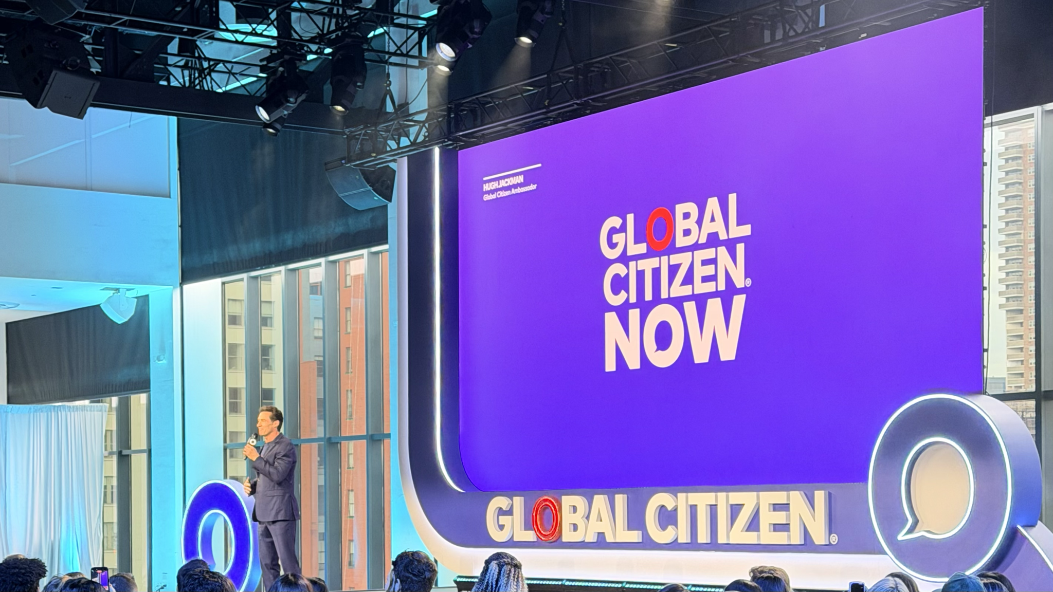 Global Citizen NOW stage with speaker in front of a large purple screen