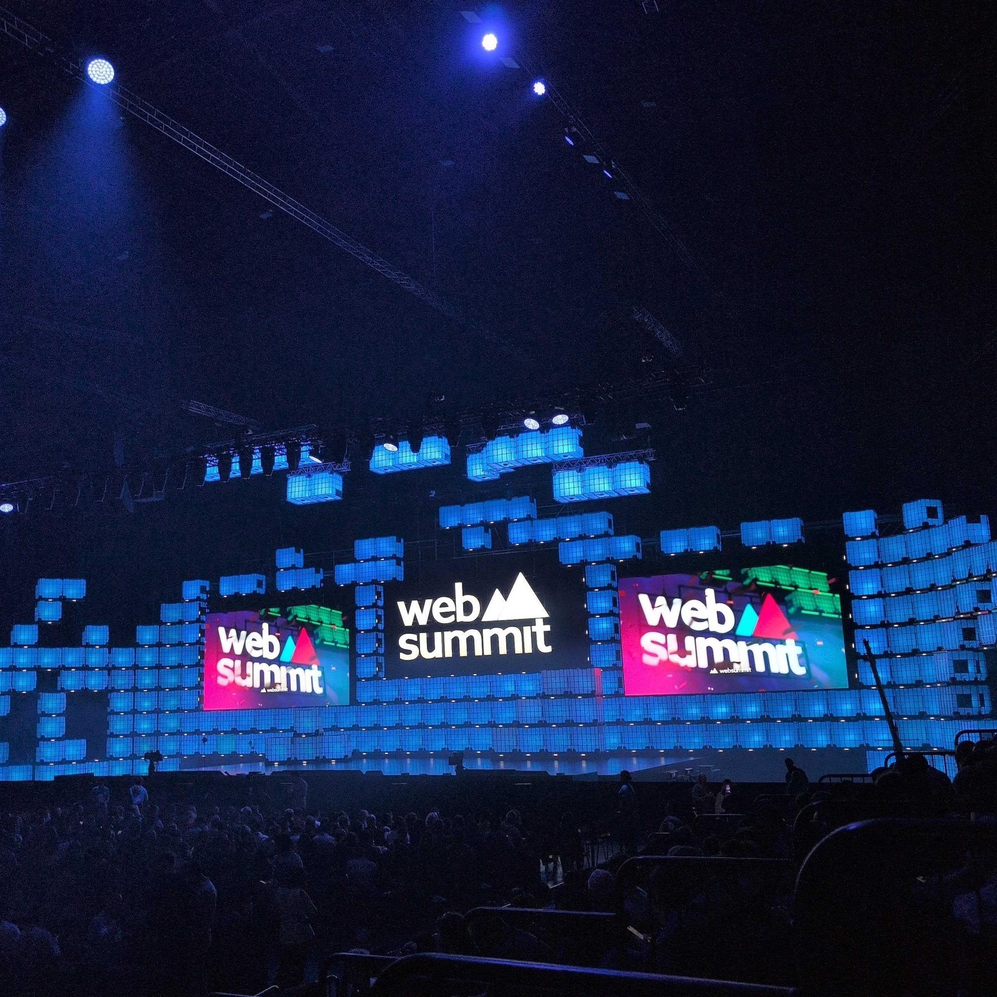 Web Summit stage with large screens and blue lighting in a packed venue