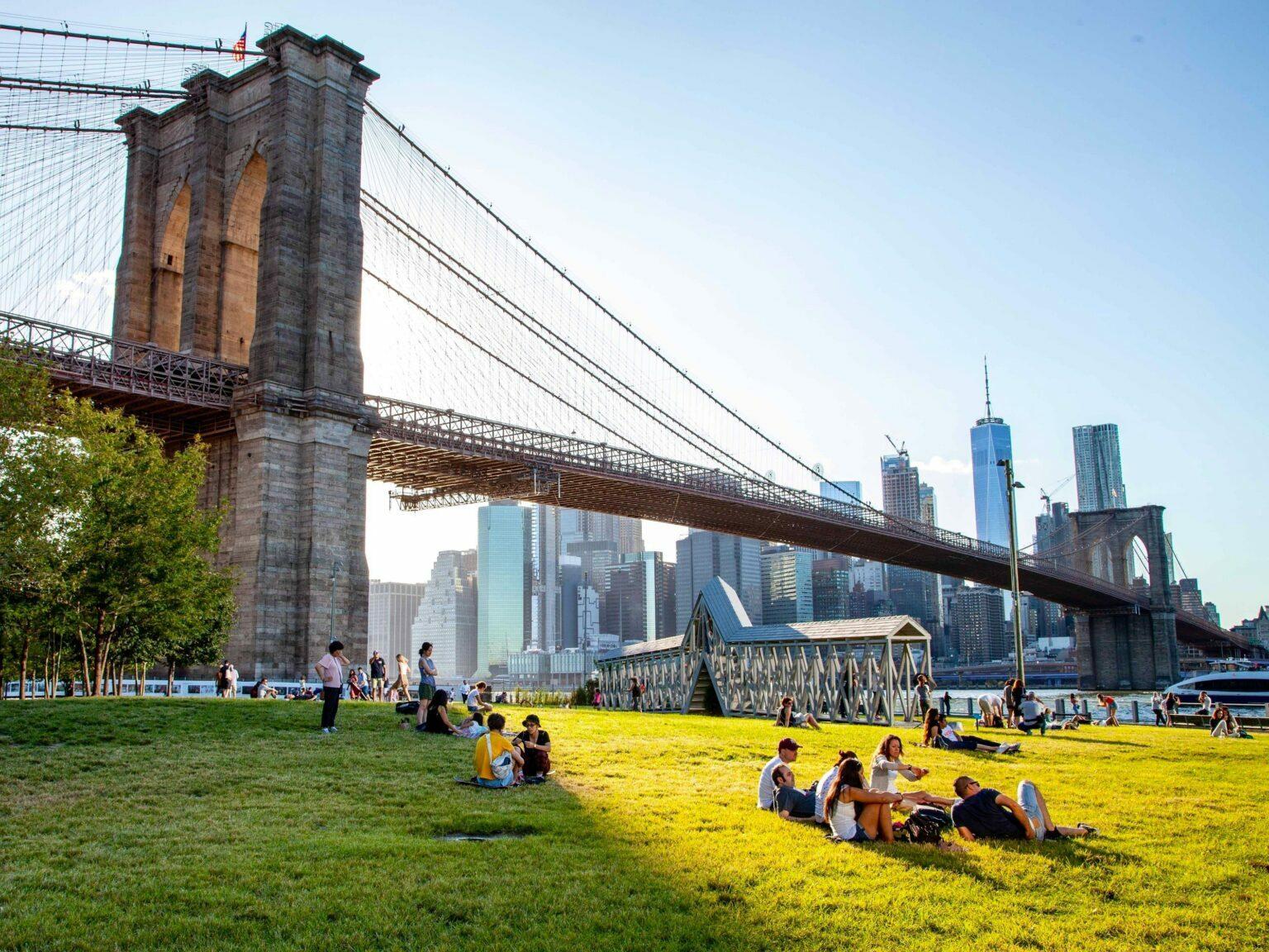 Brooklyn Bridge over a sunny park with Manhattan skyline in the distance