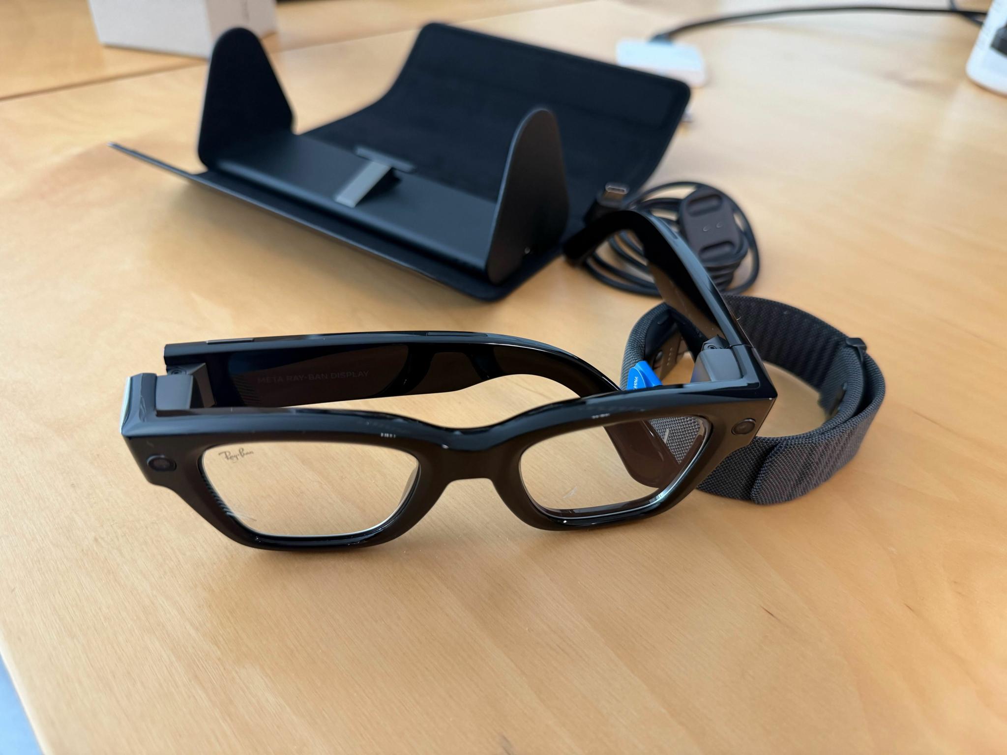 Black smart glasses and charging dock on a wooden desk