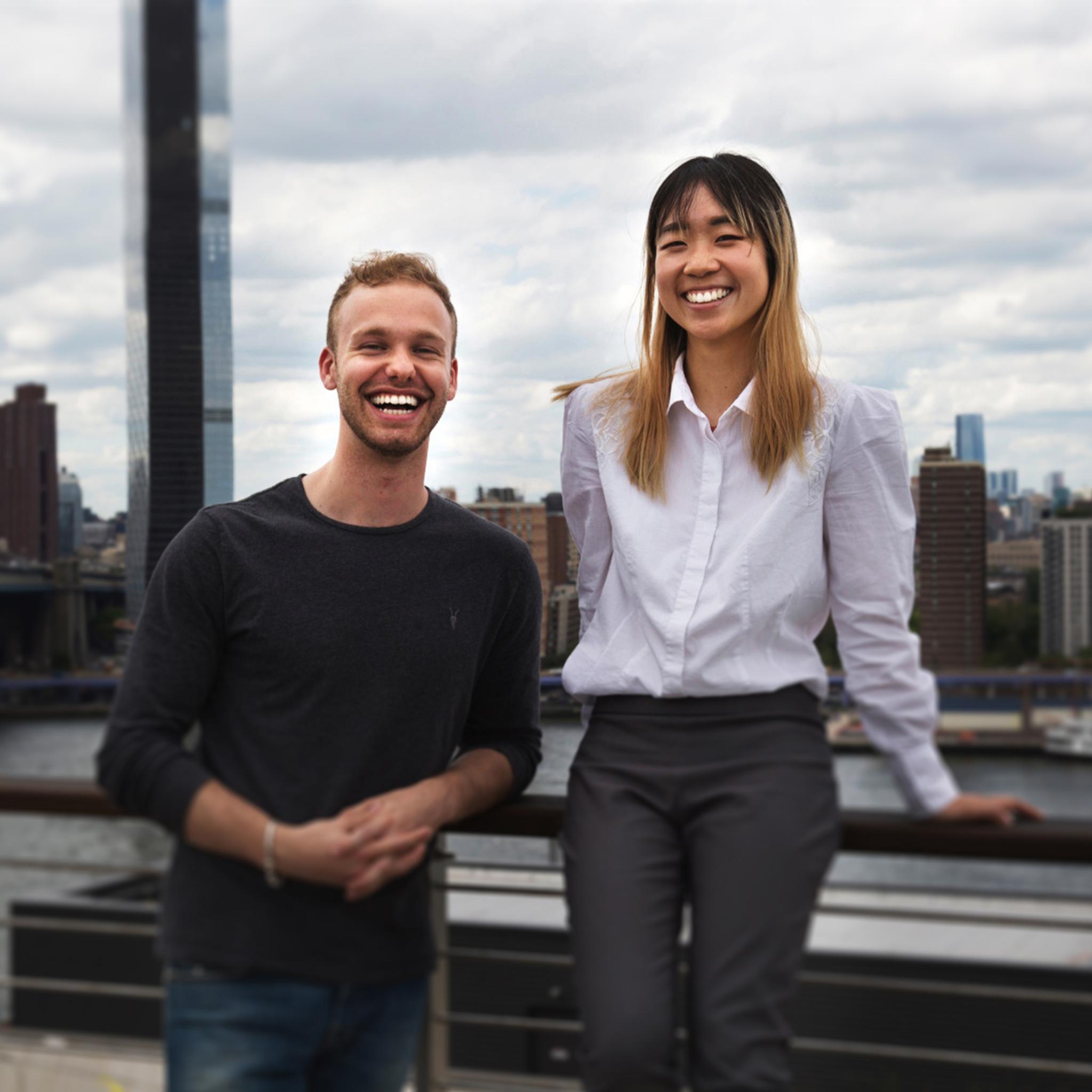 Two smiling adults on a rooftop with a city skyline behind them