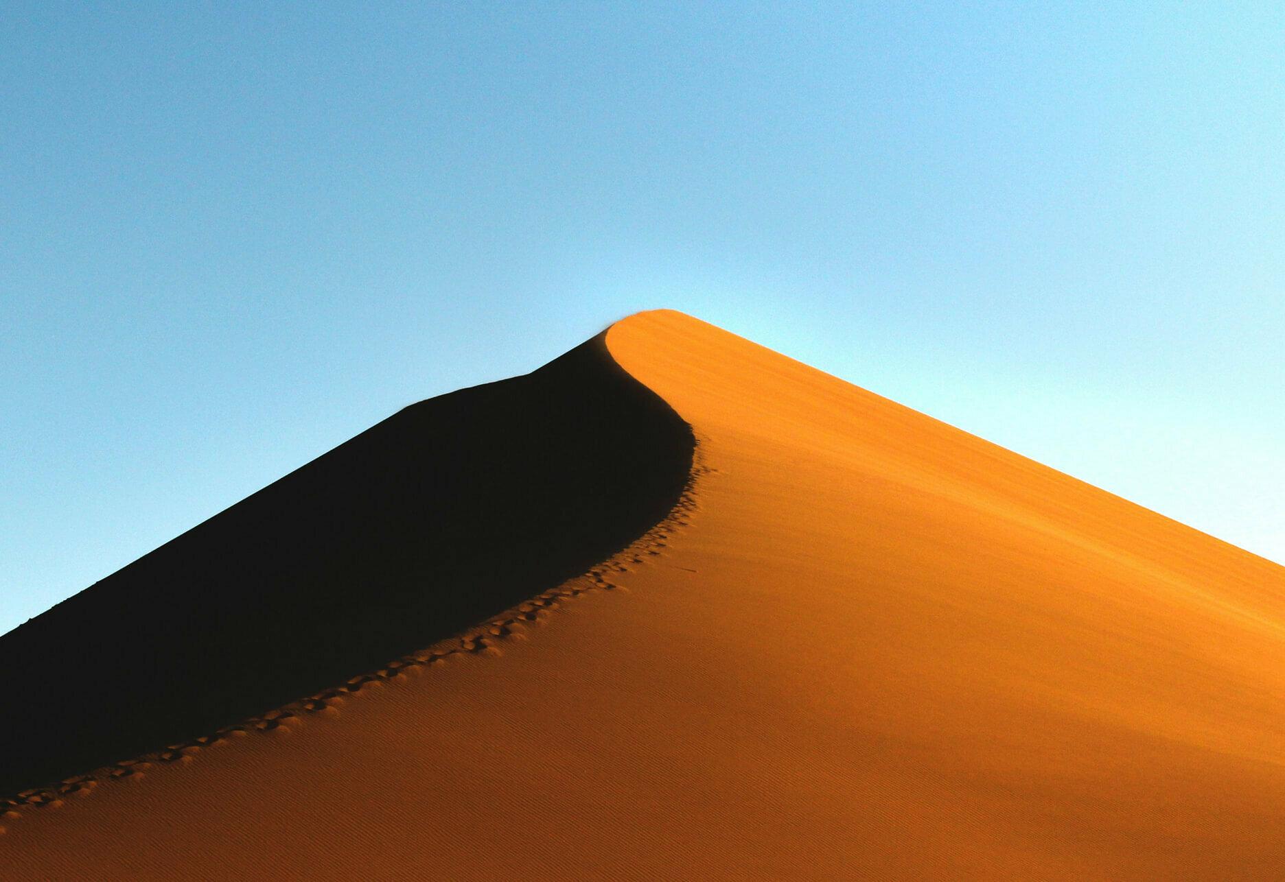 Sunlit orange sand dune ridge under a clear blue sky