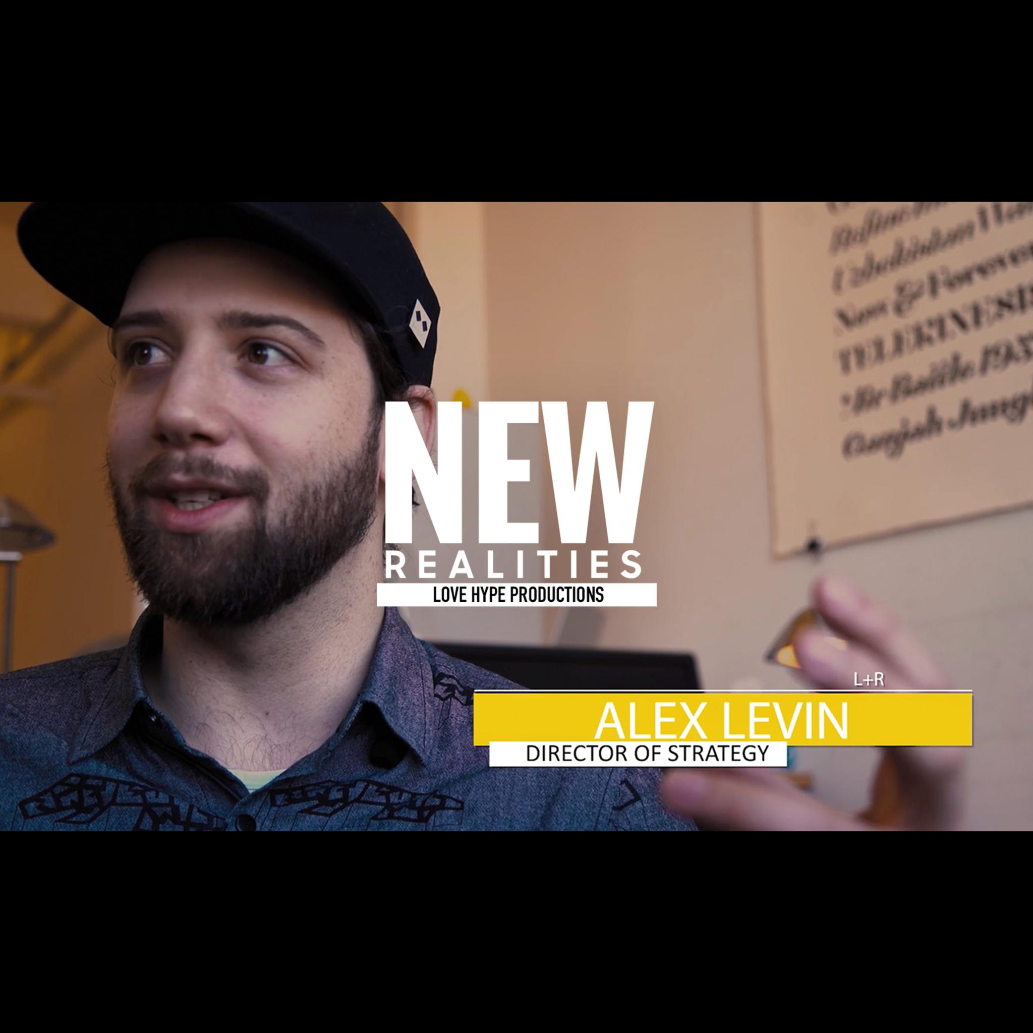 Interview still of a bearded man in a cap with "NEW REALITIES" overlay