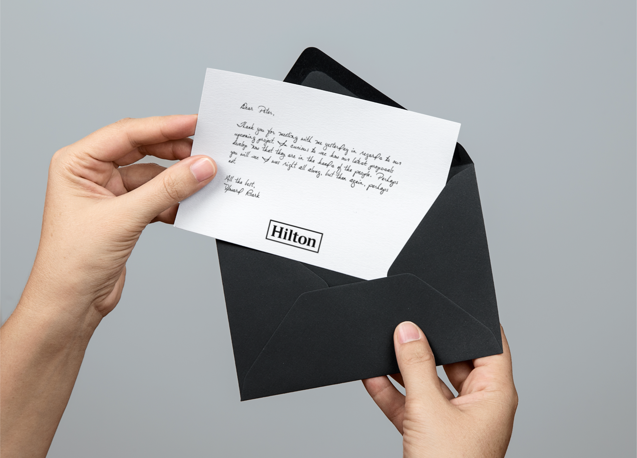 Hands holding a black envelope with a handwritten Hilton letter inside