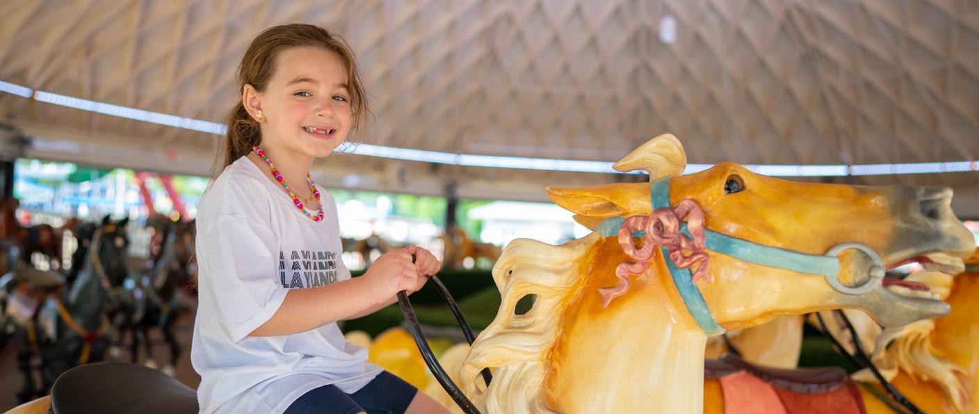 Child riding a yellow carousel horse under a covered carousel roof