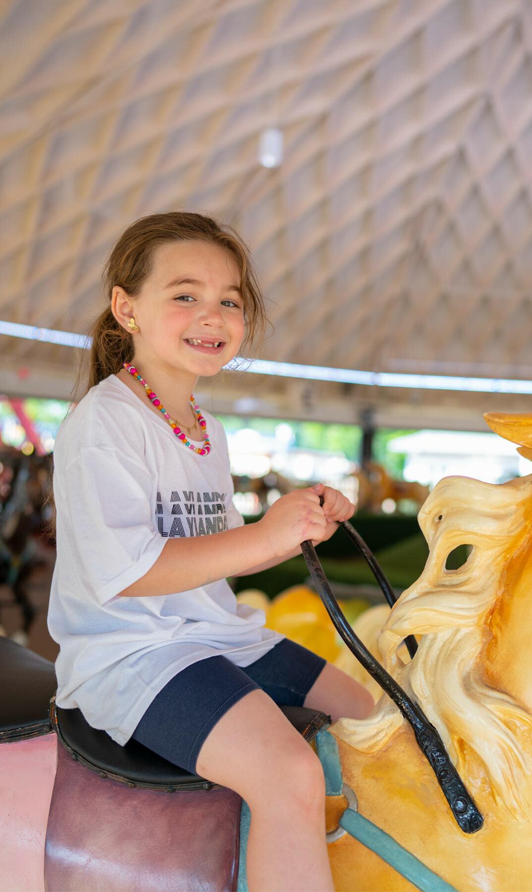 Child smiling while riding a yellow carousel horse