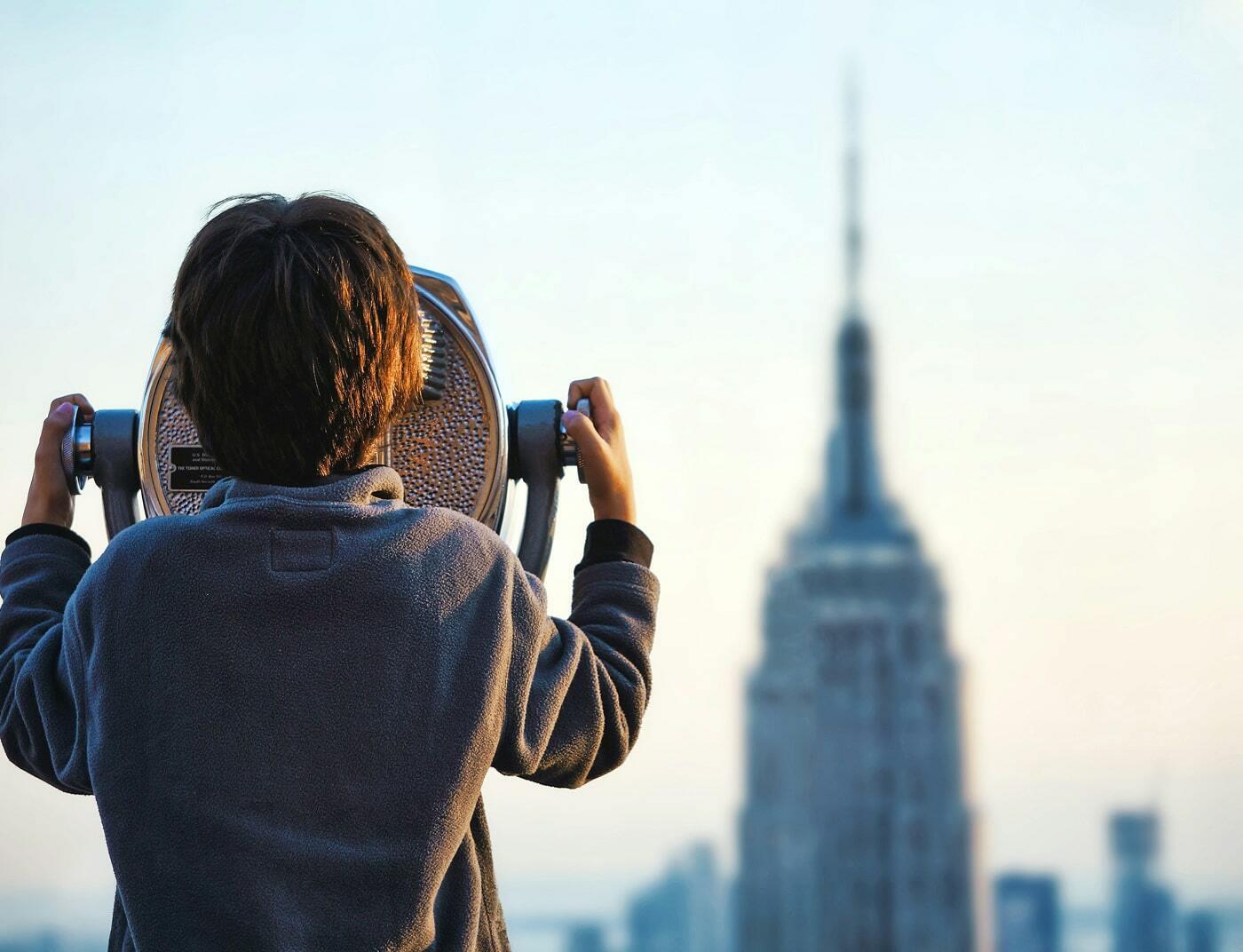 Child looking through a coin-operated viewer toward a city skyline