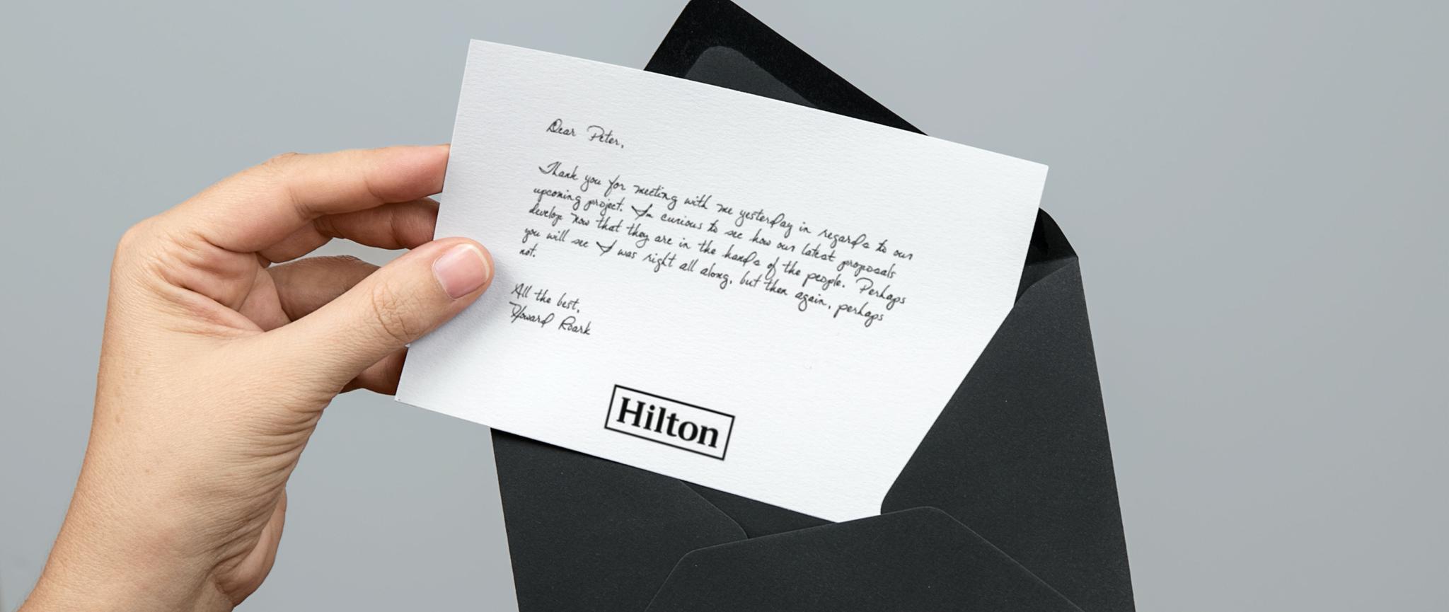 Hand holding a handwritten Hilton note above a black envelope
