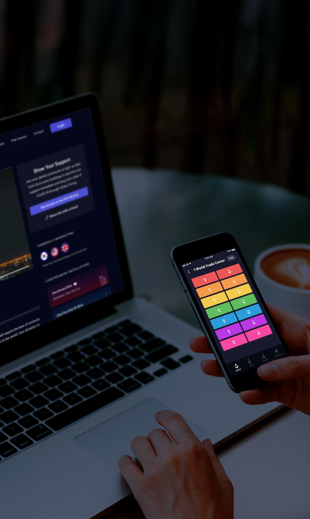 Hand holding a phone with a colorful app beside a laptop
