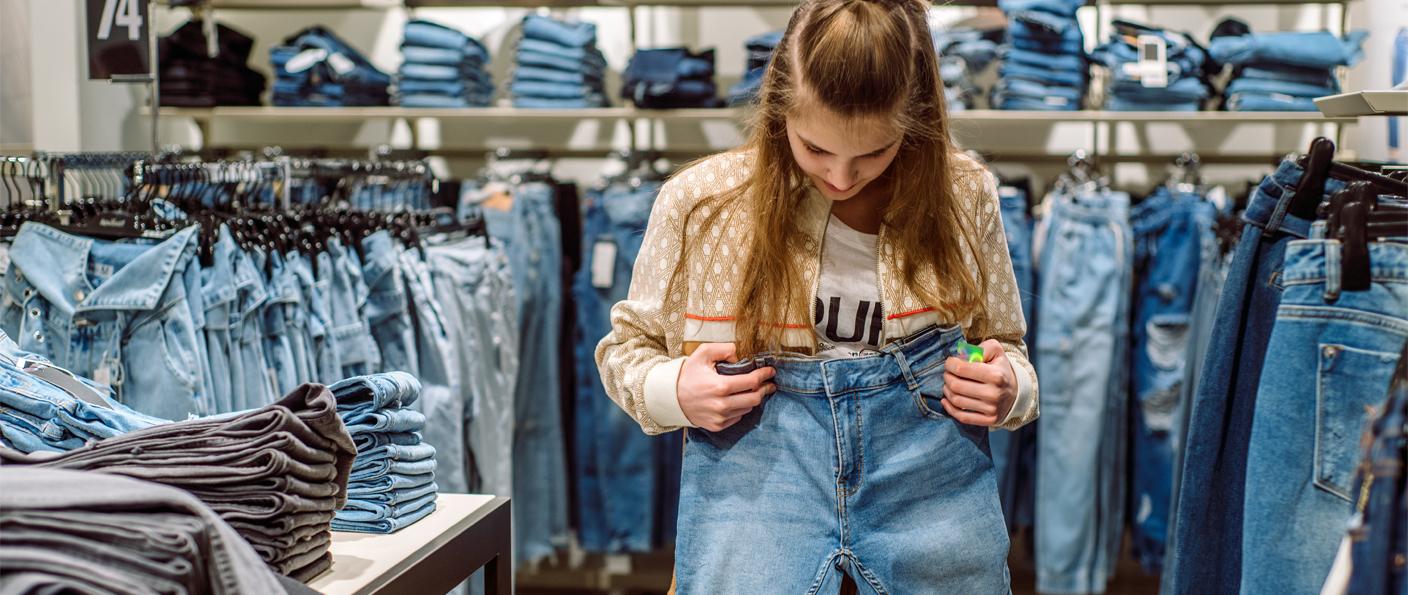 Shopper holding up jeans in a denim store aisle