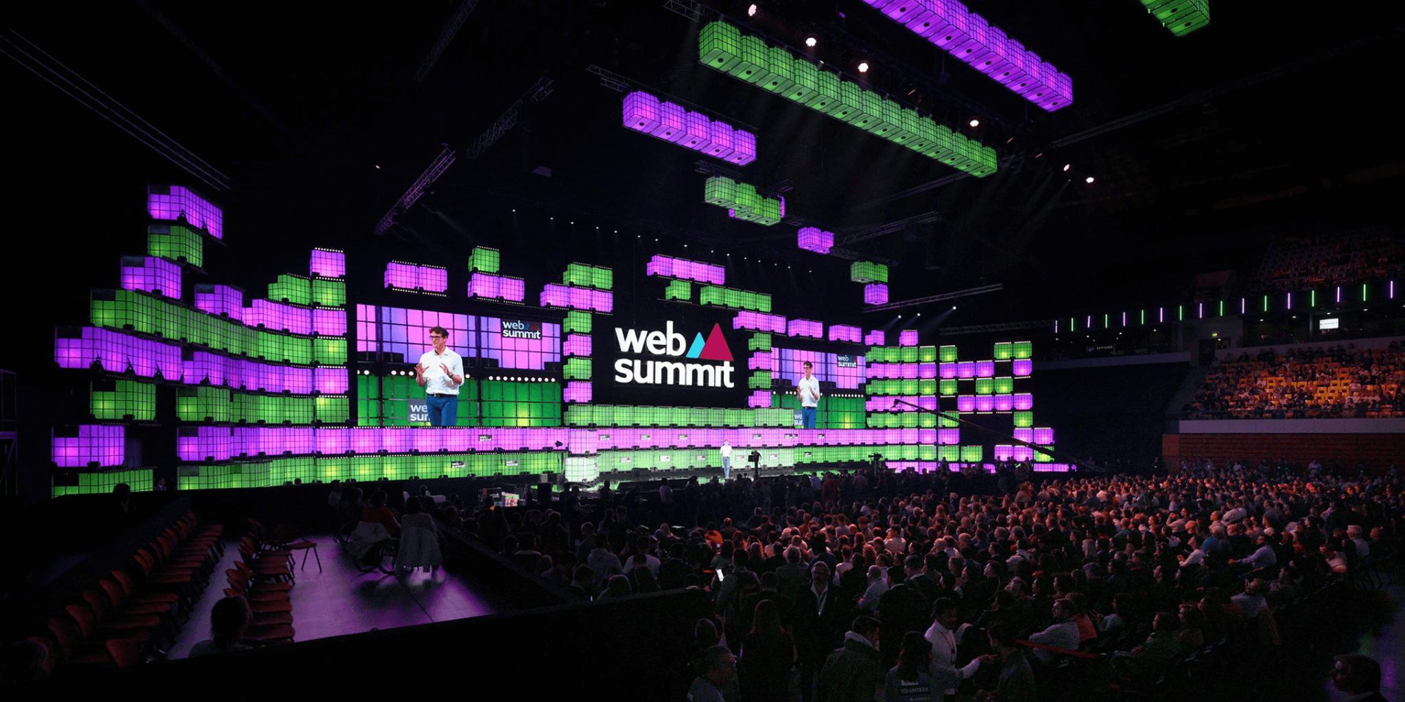 Speaker on stage at Web Summit with purple and green lights before a large audience