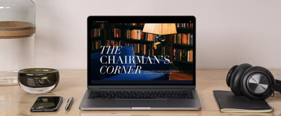 ELC Learning Hub Laptop on desk showing The Chairman's Corner, with phone, pen, headphones, notebook, and glassware