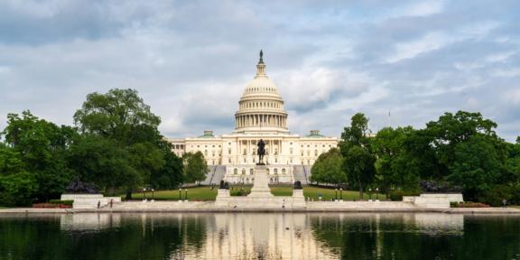 U.S. Capitol building reflected in a pool with trees and cloudy sky