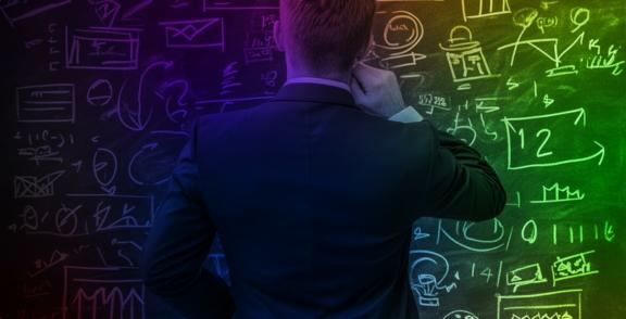 Person in a suit facing a chalkboard filled with diagrams