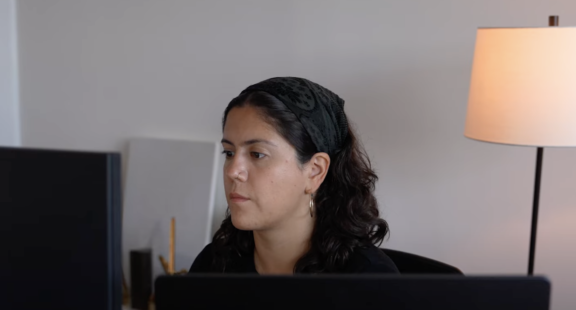 Woman working at a desk with monitors and a lamp in the background