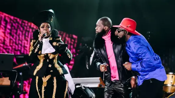 Three performers singing onstage in colorful outfits
