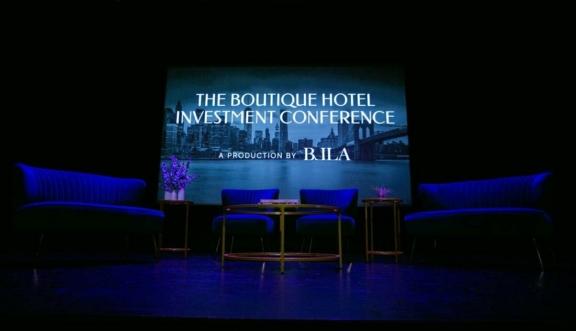 Stage setup with blue chairs and screen reading The Boutique Hotel Investment Conference