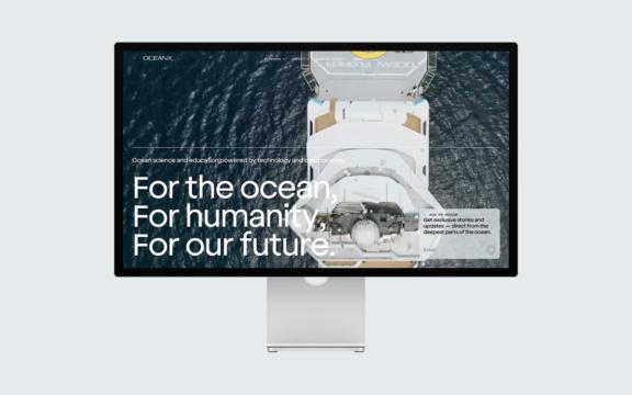 Ocean X D Featured Desktop monitor displaying an OceanX homepage over an aerial boat photo
