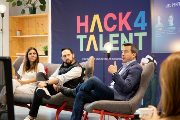 Panelists seated on stage at a Hack 4 Talent event with a colorful backdrop
