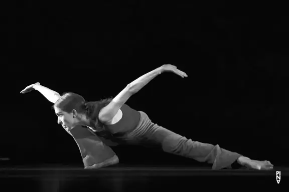 Dancer in a low, extended pose on a dark stage in black and white