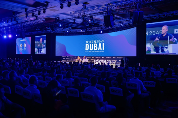 TOKEN2049 Dubai conference hall with audience, stage screens, and panel speakers