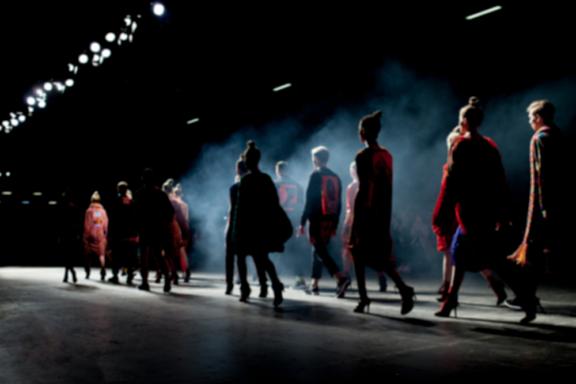 Models walk a dimly lit runway with stage smoke