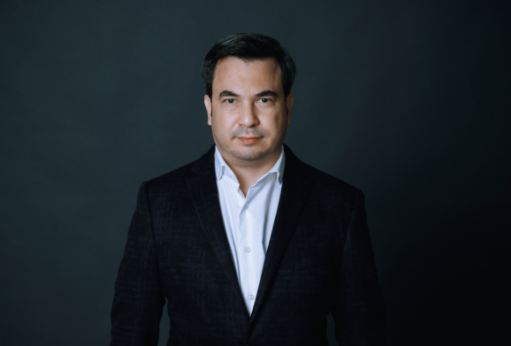 Man in a dark blazer against a dark background