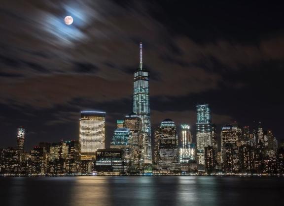 New York City skyline at night with One World Trade Center and a cloudy moon