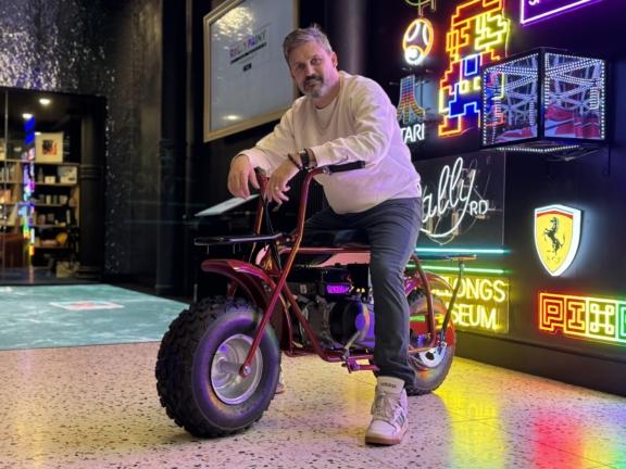 Person posing on a red minibike beside neon arcade and Ferrari signs