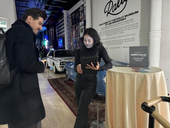 Two attendees using a tablet near cars and a Sporting Crypto Social sign
