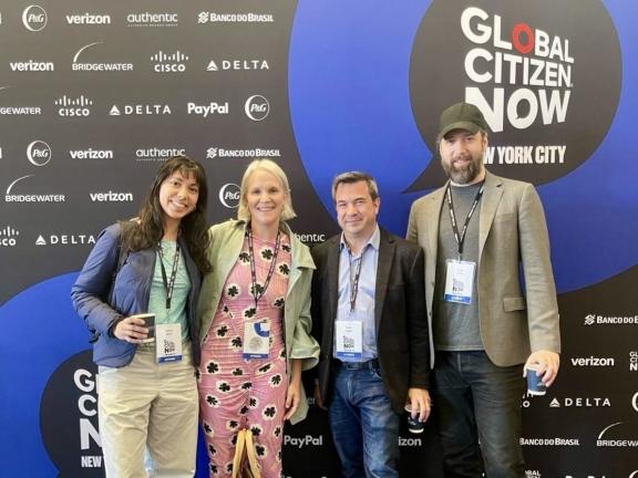 Four attendees posing in front of a Global Citizen NOW New York City sponsor backdrop