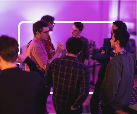 Group of people chatting in a purple-lit room during a networking event