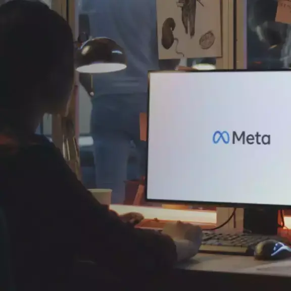 Person at a desk facing a monitor displaying the Meta logo