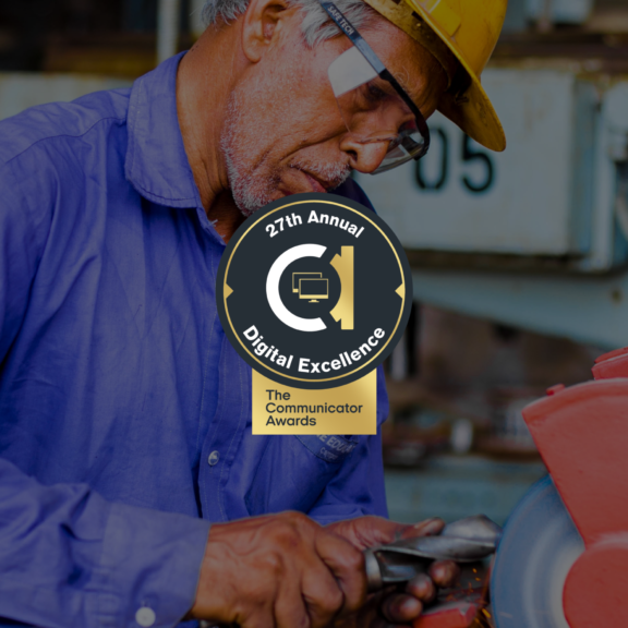 Industrial worker using a tool with a Communicator Awards Digital Excellence badge overlay.