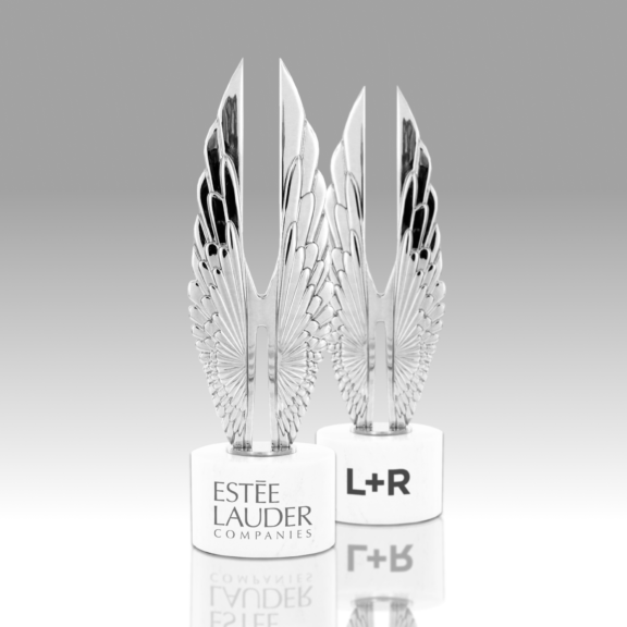 Two silver wing-shaped trophies on white bases labeled Este Lauder and L+R