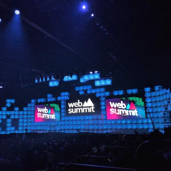 Web Summit stage with large screens and blue lighting in a packed venue