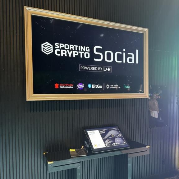 Framed Sporting Crypto Social powered by L+R sign above a kiosk
