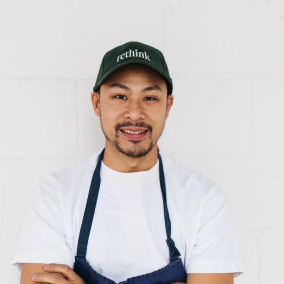 Portrait of a person wearing a rethink cap and apron against a white wall