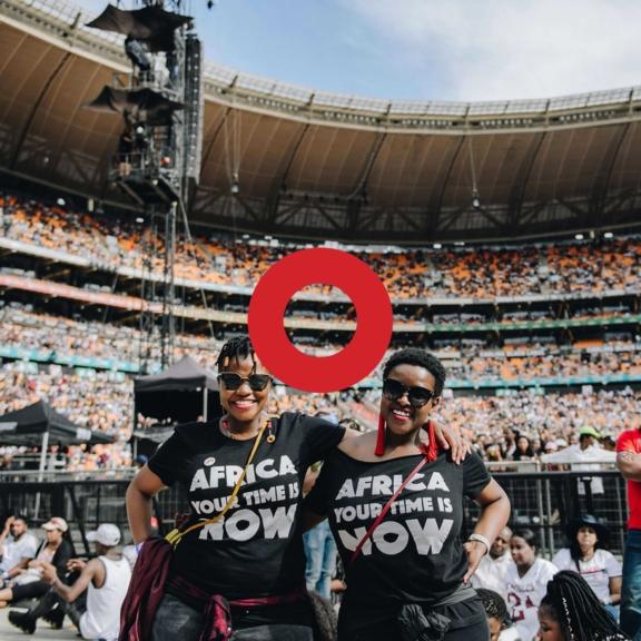 Two women in Africa Your Time Is Now shirts in a crowded stadium with a red ring overlay