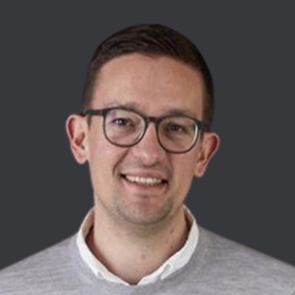Timur Smiling man with glasses in a gray sweater against a dark background