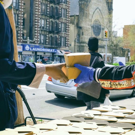 Person handing stacked takeout boxes to a gloved hand near a table of boxes