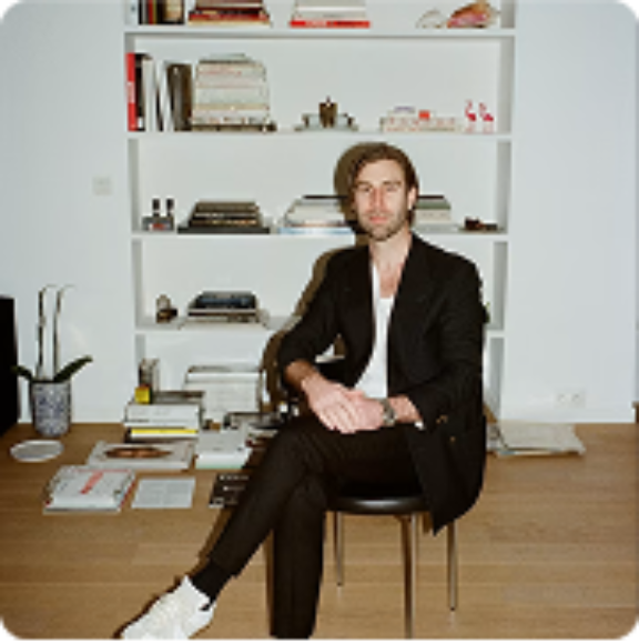 Cameron lamb Person in a black suit seated in an office with shelves and papers
