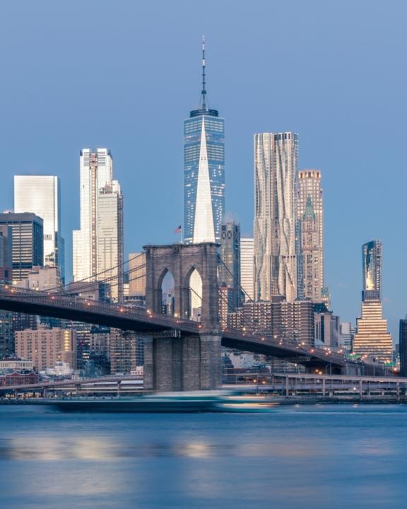 Brooklyn Bridge with Lower Manhattan skyline and One World Trade Center at dusk