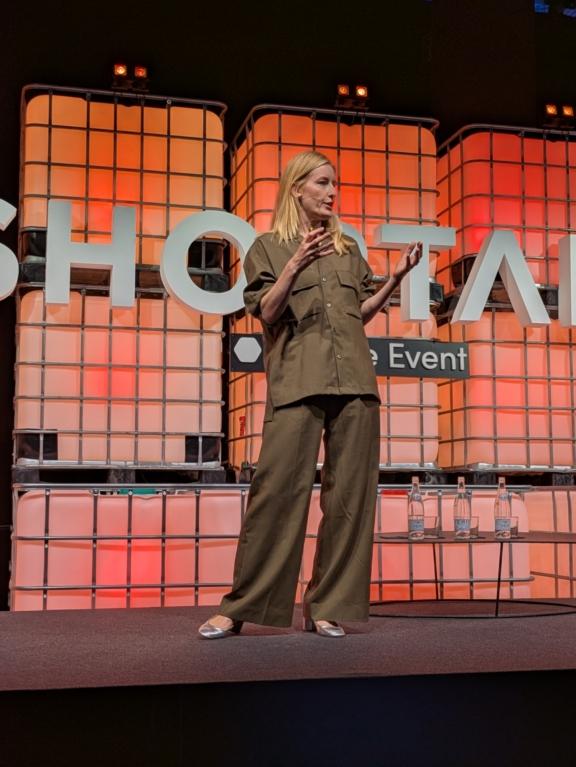 Woman speaking on a Shoptalk stage with orange backdrop