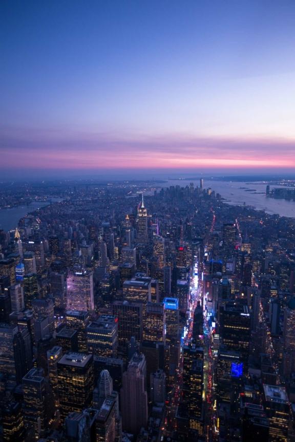 Aerial view of New York City at dusk with lit skyscrapers and river