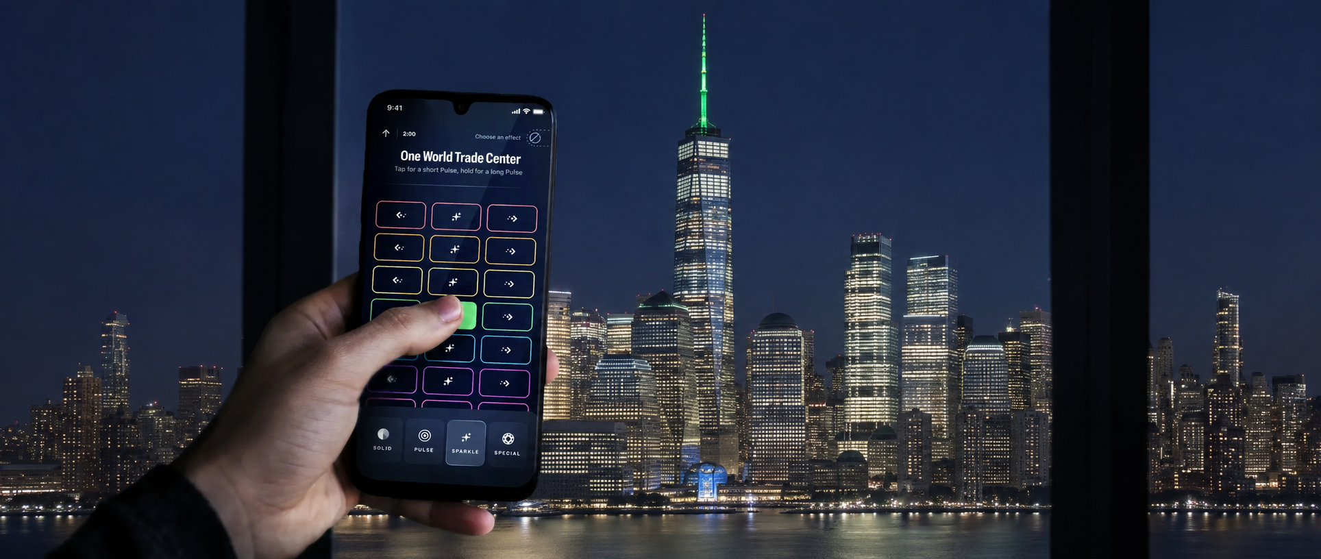 Hand holding a phone controlling One World Trade Center lights at night