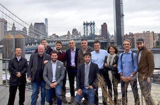 Group of adults posing outdoors by the Manhattan Bridge and city skyline