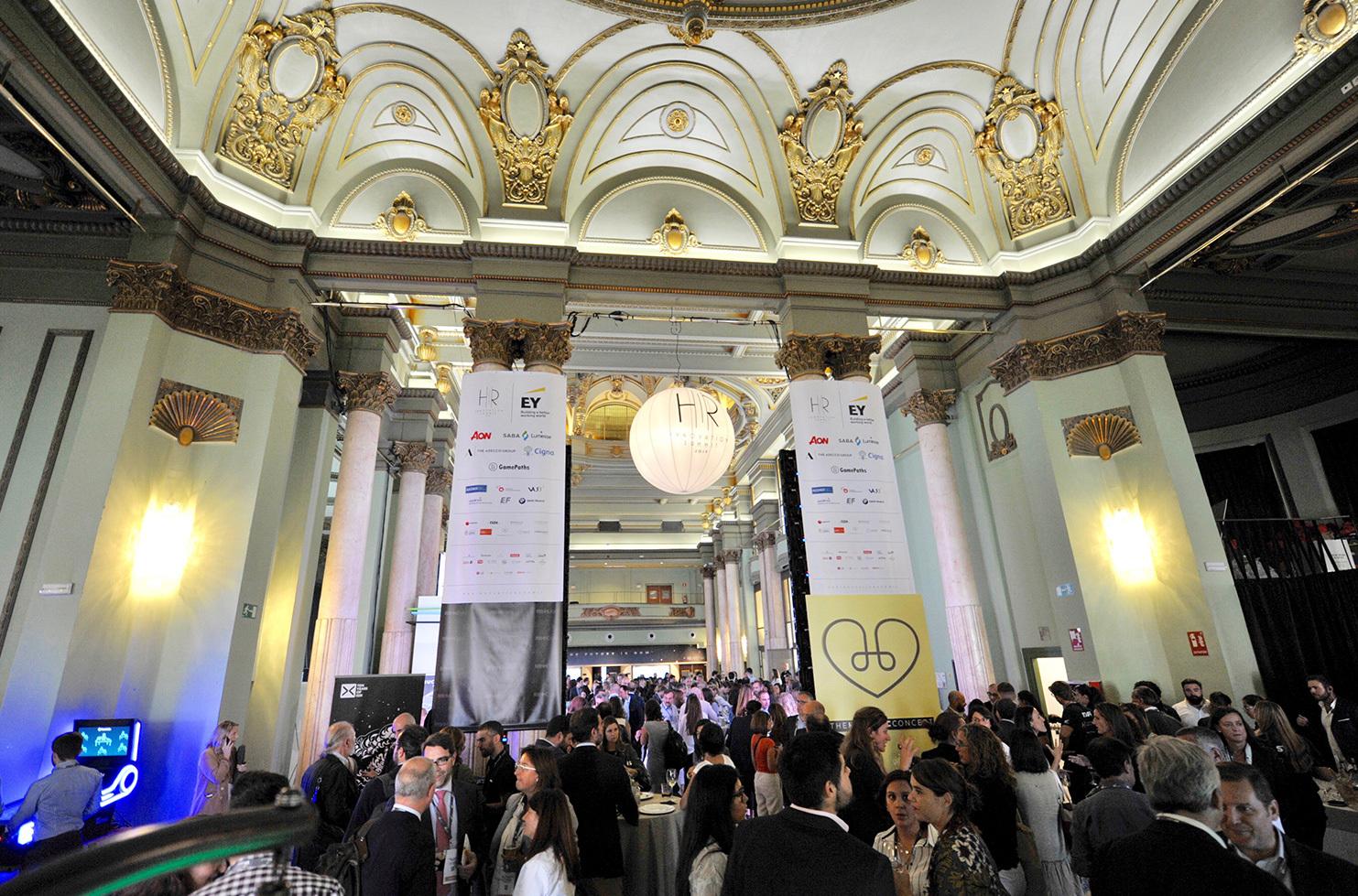 Crowd networking inside an ornate conference hall with sponsor banners