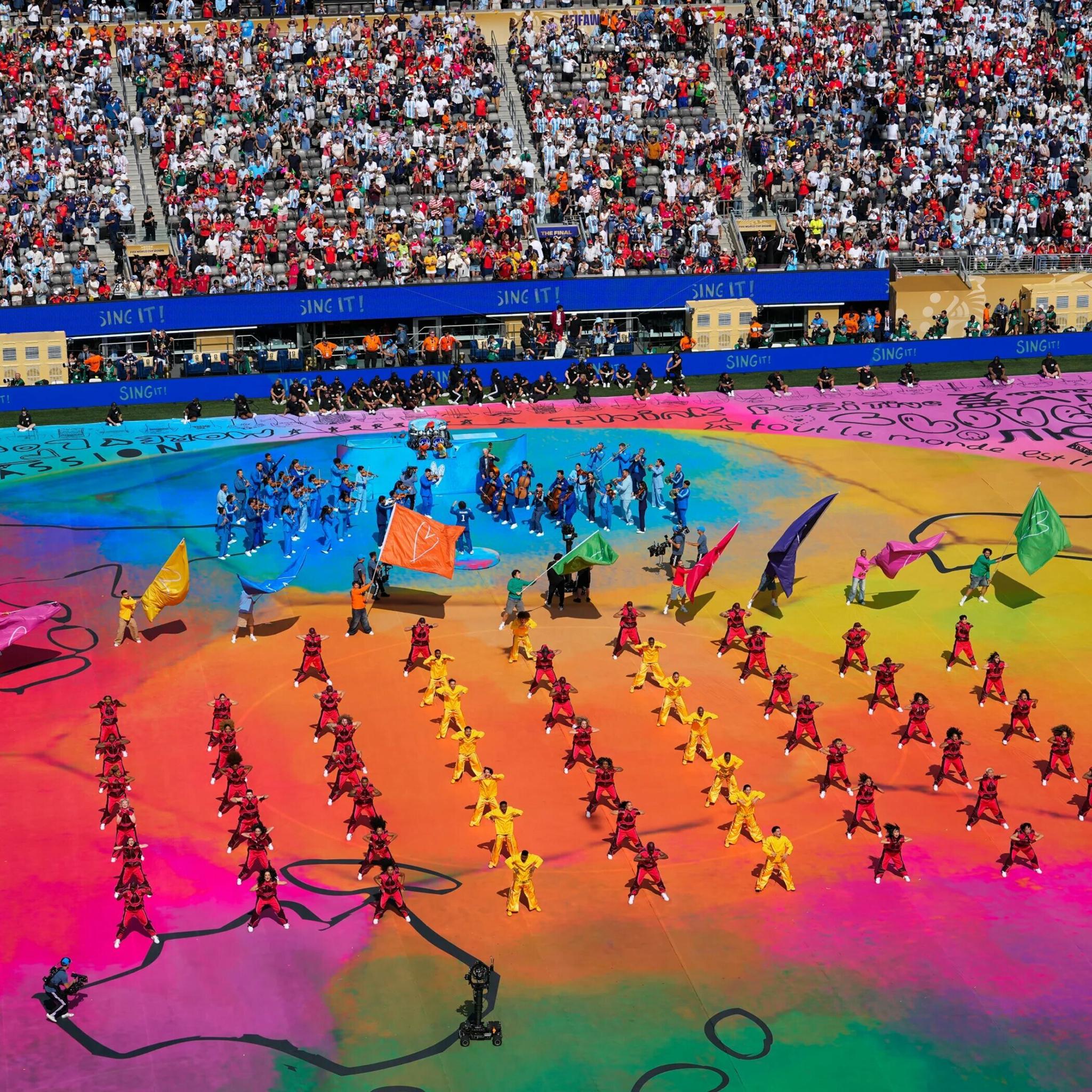 Performers form colorful patterns across a packed stadium field.