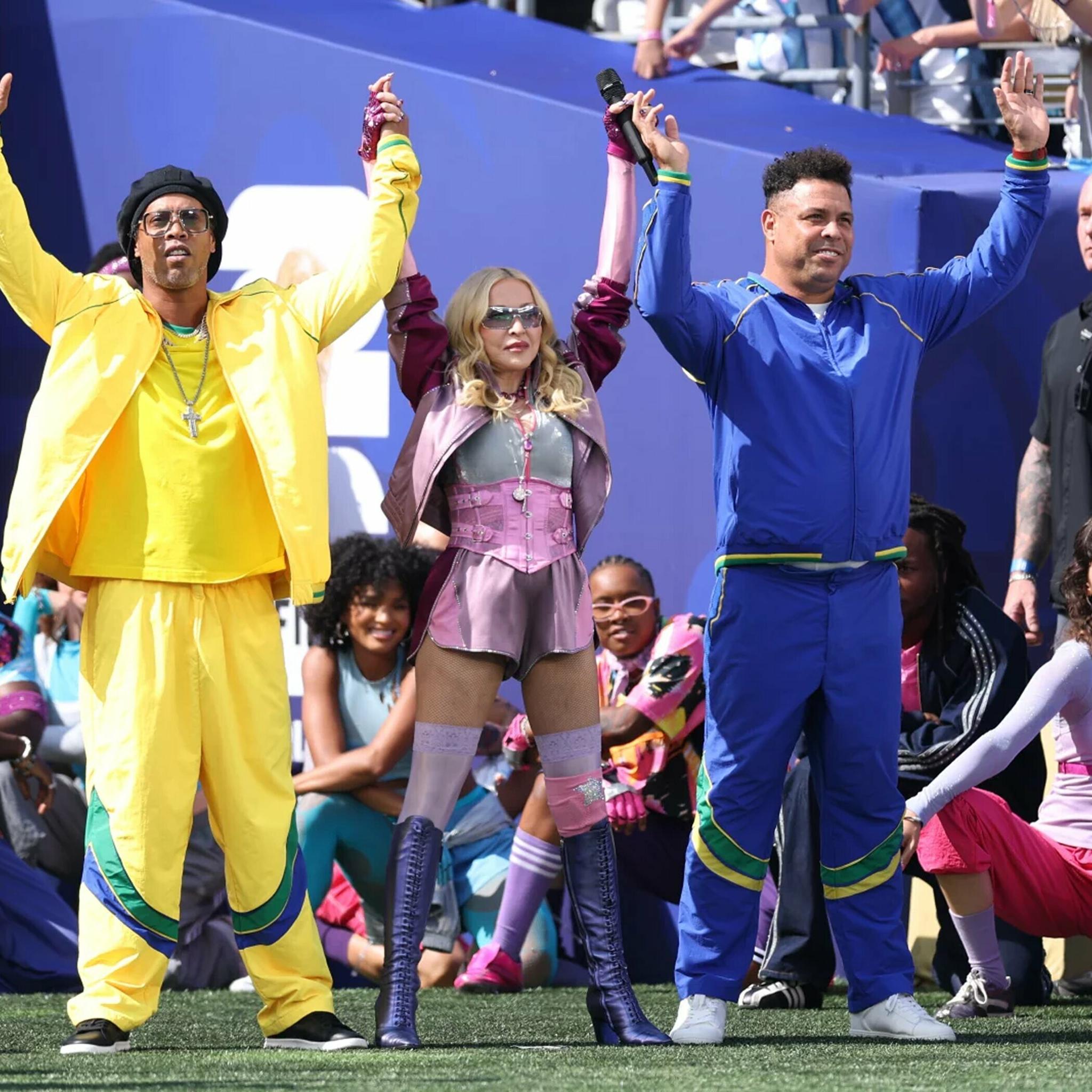 Performers in yellow, pink, and blue costumes wave on a stadium field.